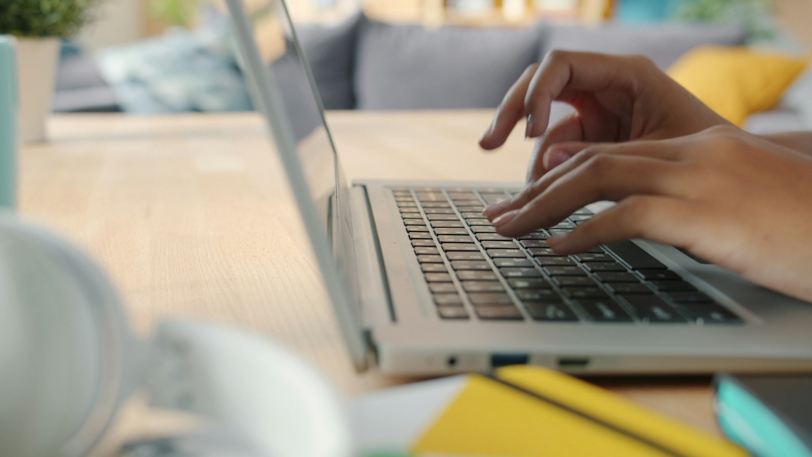Kädet kirjoittavat kannettavan tietokoneen näppäimistöllä päivänvalossa.
